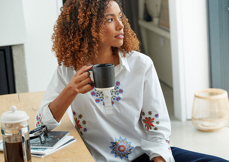 Woman wearing white printed tunic top with a mug in hand