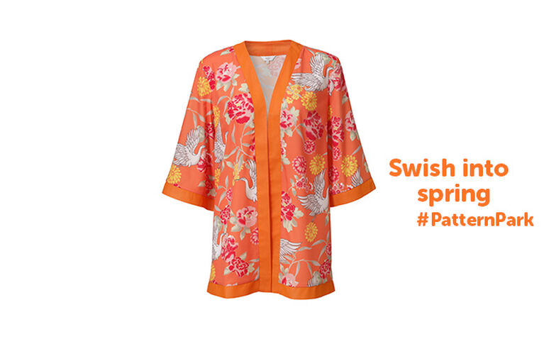 A product shot of an orange kimono that has a floral and bird print on it