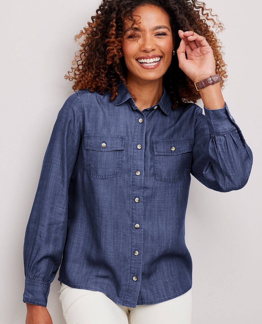 Woman laughing wearing a button-up blue denim blouse with white jeans