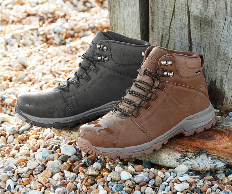 A still shot photograph of a pair of the Cotton Traders Hydroguard® Walking Boots on a stoney beach