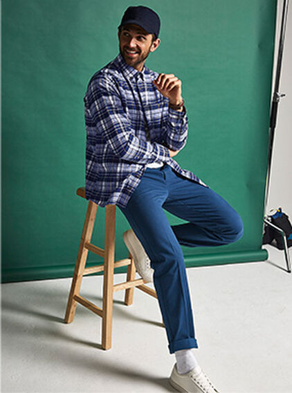 Man sitting down on a stool wearing the Cotton Traders Check Shirt and Chinos