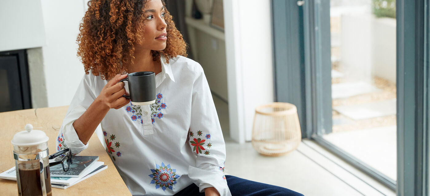Woman wearing white printed tunic top with a mug in hand