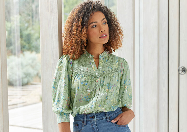 Woman looking off to the side wearing a green button-up blouse and blue jeans